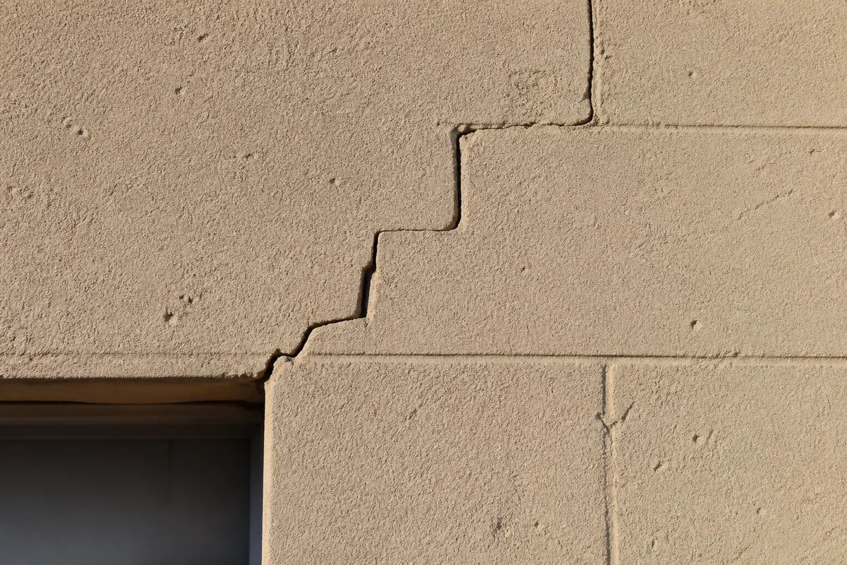 Fissure en escalier sur un mur de maçonnerie près d’une ouverture, lumière rasante